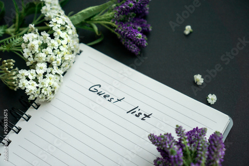 Handwritten text guest list with black background, violet and white flowers  photo