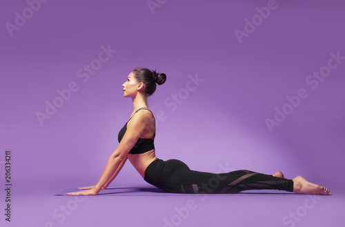 Long haired beautiful pilates or yoga athlete does a graceful pose while wearing a tight sports outfit against a bright purple background in a studio photo