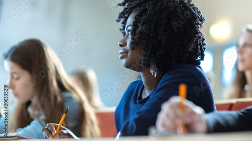 Close-up of a Beautiful Black Female Student Sitting Among Her Fellow Students in the Classroom, She's Writing in the Notebook and Listens to a Lecture.