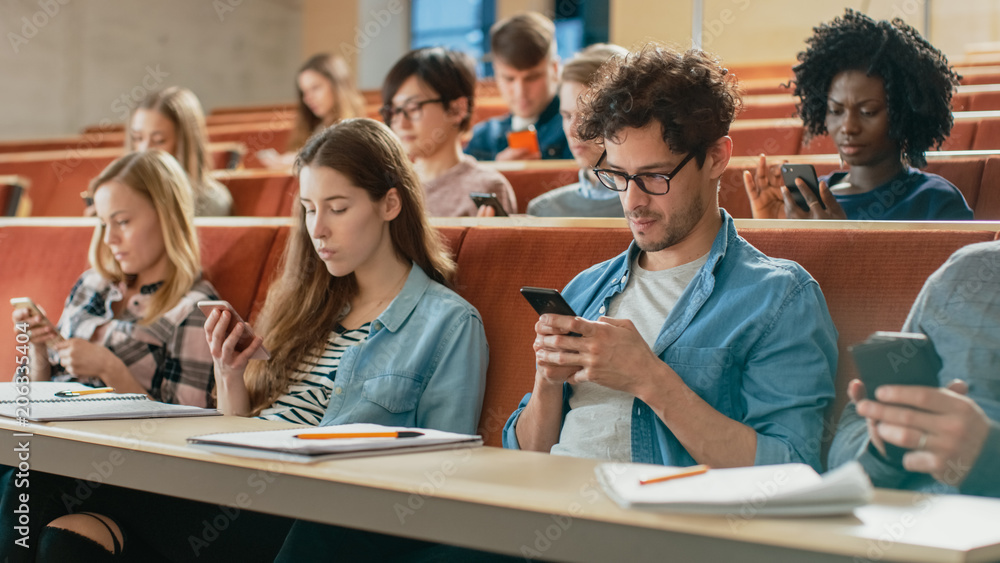 Obraz premium Wieloetniczna grupa studentów korzystających ze smartfonów podczas wykładu. Młodzi ludzie korzystający z mediów społecznościowych podczas studiów na uniwersytecie.