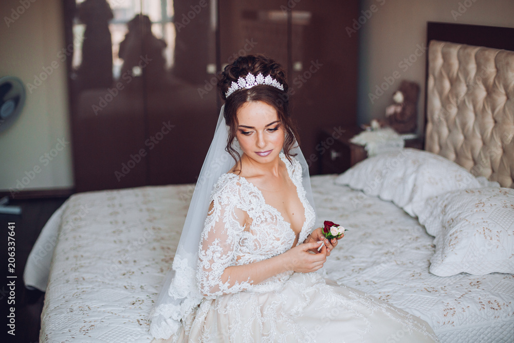 Fototapeta premium Attractive young bride holding the groom's buttonhole. flowers with pink roses, white carnation and green and greens. Bride's Preparations. Wedding Morning.