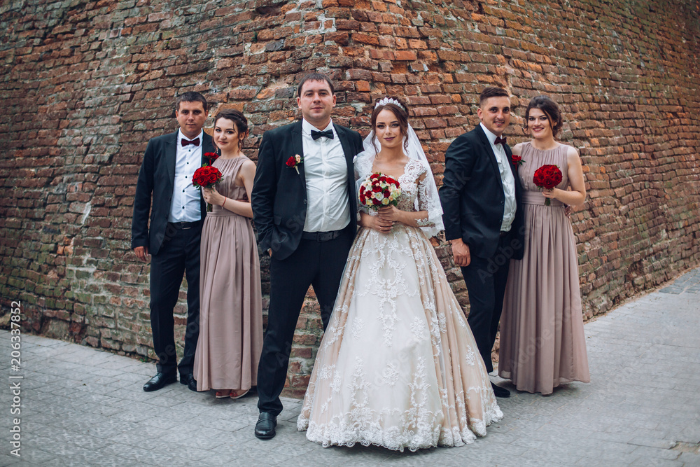 Newlyweds and their friends before wedding caremony have fun posing before an old wall. Bride and groom with bridesmaids and gromsmen on wedding photosession. Newlyweds and their friends before wedding caremony have fun posing before an old wall. Bride and groom with bridesmaids and gromsmen on wedding photosession.