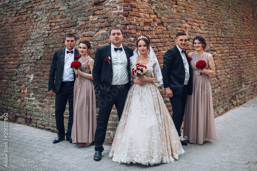 Newlyweds and their friends before wedding caremony have fun posing before an old wall. Bride and groom with bridesmaids and gromsmen on wedding photosession.  photo