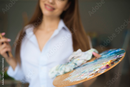 Portrait of talented young woman painting picture in art studio with inspiration