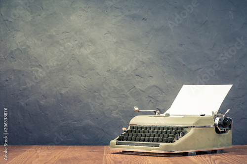 Retro typewriter with sheet of paper on wooden table front black concrete wall background. Vintage style filtered photo