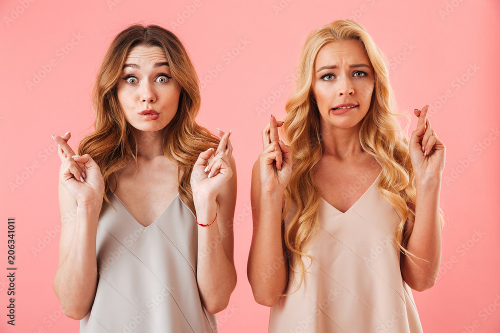 Two worried pretty women in pajamas praying with crossed fingers Two worried pretty women in pajamas praying with crossed fingers