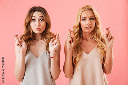 Two worried pretty women in pajamas praying with crossed fingers