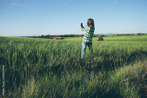 Mujer joven en una pradera verde sacando fotos con su teléfono móvil 