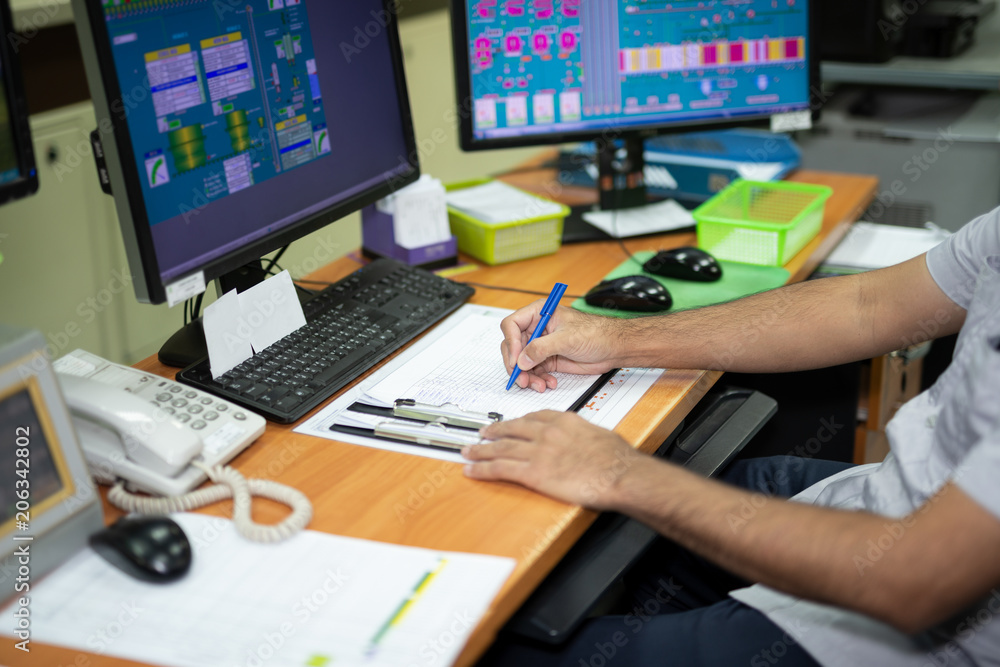 Male employees write notes work in production control room. There is a computer in the control of machinery at feed mills. Male employees write notes work in production control room. There is a computer in the control of machinery at feed mills.