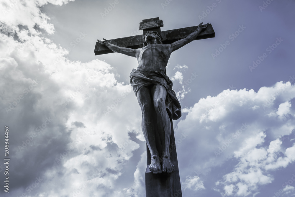 Antique crucifix, lit by the sun, against the sky with clouds