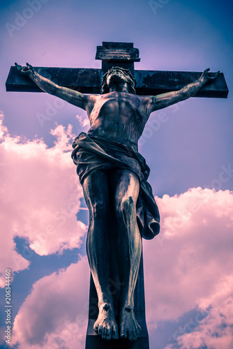 Antique crucifix, lit by the sun, against the sky with clouds