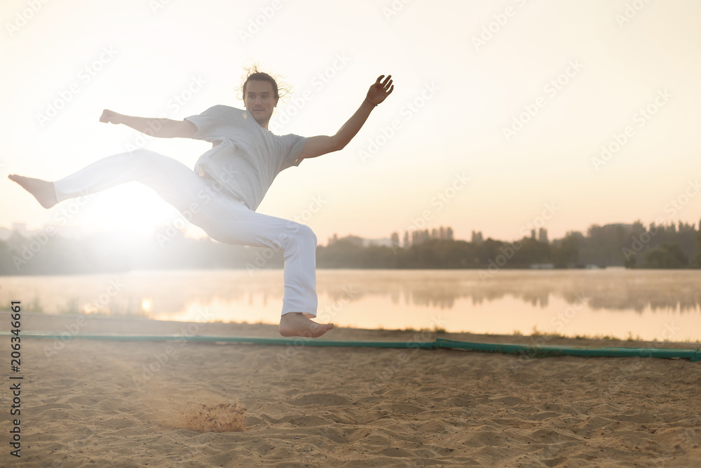 Fototapeta premium Athletic capoeira performer workout training on the beach sunris