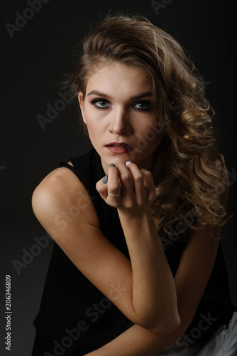 Close up portrait of attractive blonde woman with beautiful make up wearing black blouse posing isolated against black background in the studio