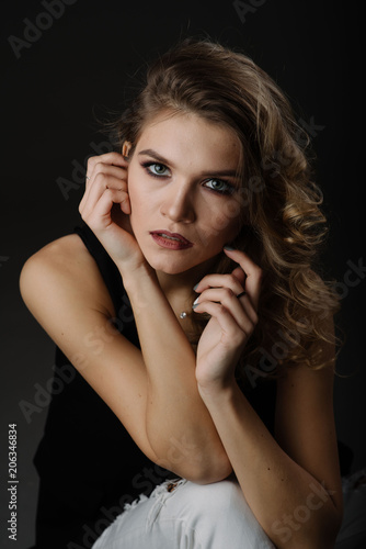 Close up portrait of attractive blonde woman with curly hairstyle, beautiful make up, wearing black blouse posing isolated on black background