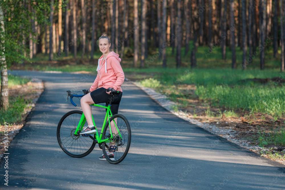 Obraz premium Girl on a bicycle in a pink hoodie in the park. Races on a bicycle. Active way of life and playing sports.