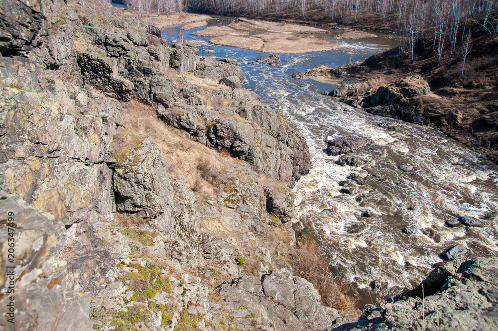a rough river with rapids in the forest, with splashes of water, under a blue sky, surrounded by forest