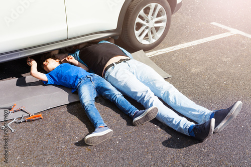 Father teaching son to repair car lying under auto