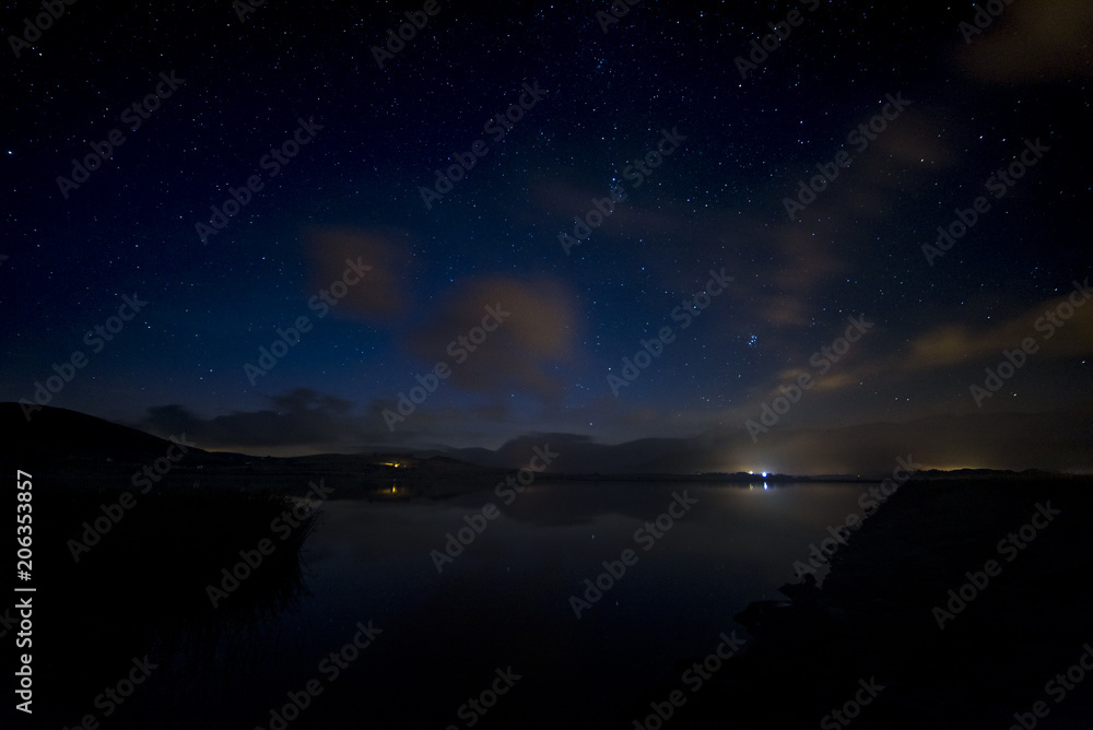 Night sky with stars and clouds over lake