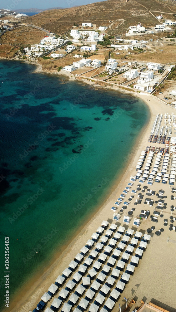 Aerial drone bird's eye view photo of famous organized with sun beds emerald clear water beach of Ornos in island of Mykonos, Cyclades, Greece