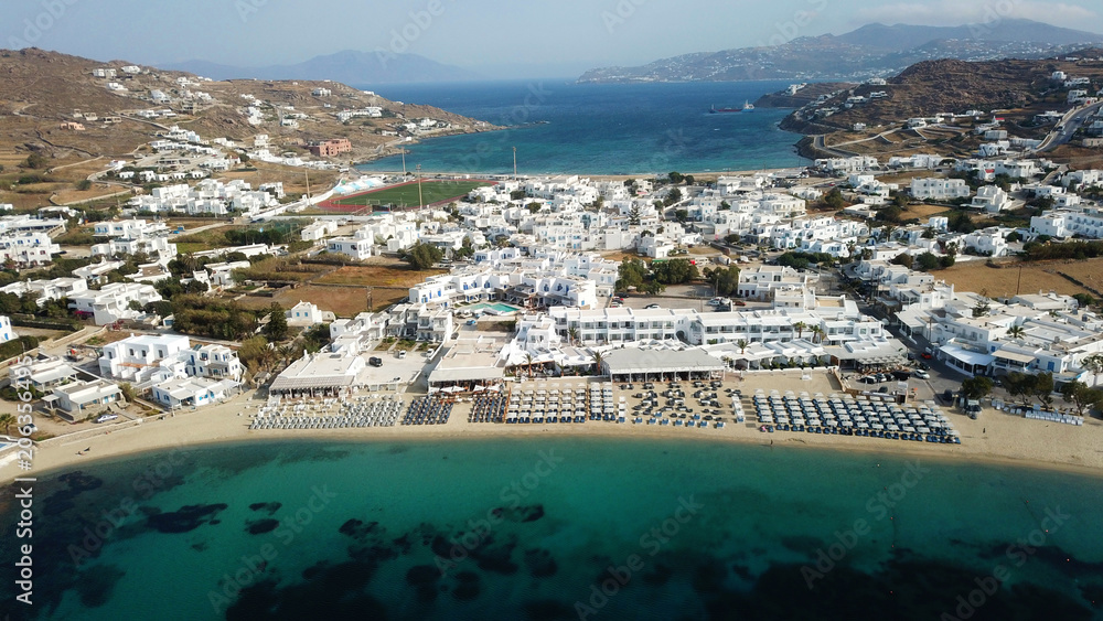 Aerial drone bird's eye view photo of famous organized with sun beds emerald clear water beach of Ornos in island of Mykonos, Cyclades, Greece
