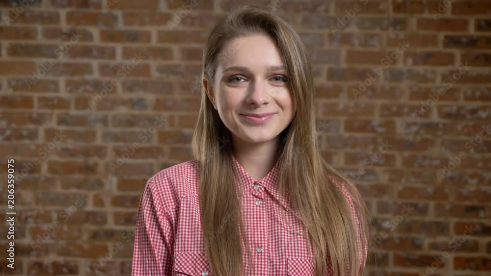 Young blonde is smiling, grin, watching at camera, brick background. Young blonde is smiling, grin, watching at camera, brick background.