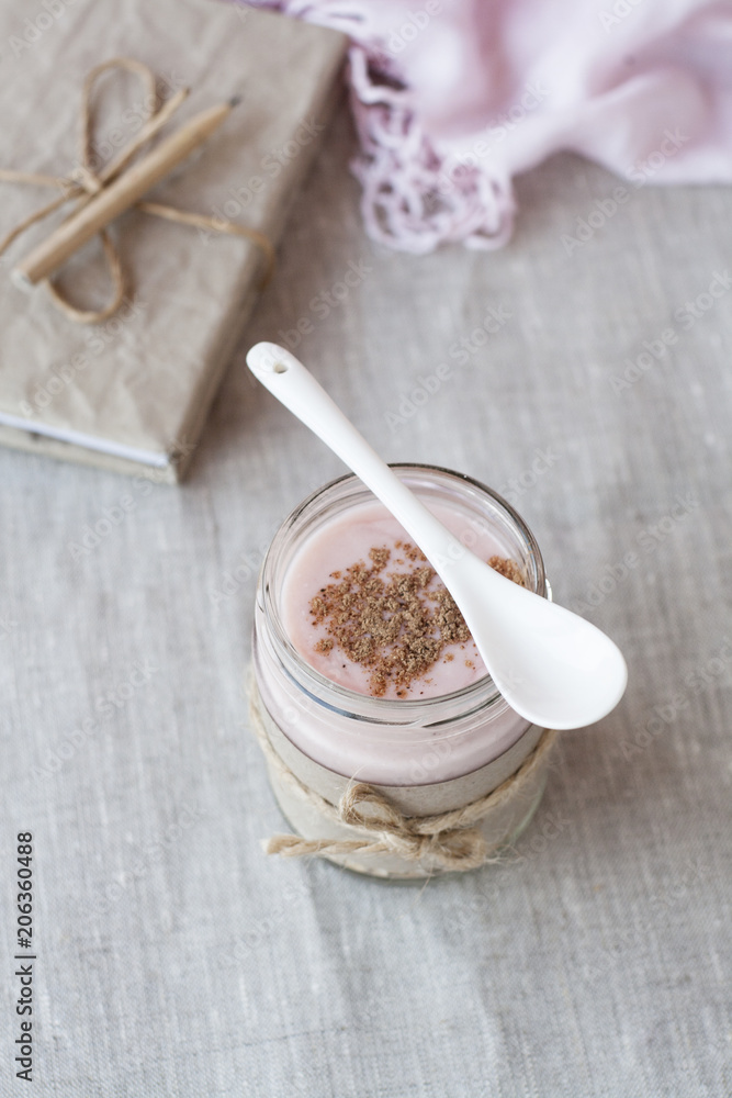 Fototapeta premium Oatmeal, flavored with yogurt, sprinkled with cinnamon in a glass jar. Next is a craft notebook and a pink napkin.
