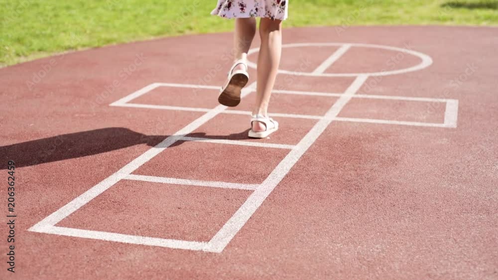 Little girl jumping while playing Hopscotch at park. Cute girls on children playground outdoors. Legs of kids jumps hopscotch on asphalt. Little girl jumping while playing Hopscotch at park. Cute girls on children playground outdoors. Legs of kids jumps hopscotch on asphalt.