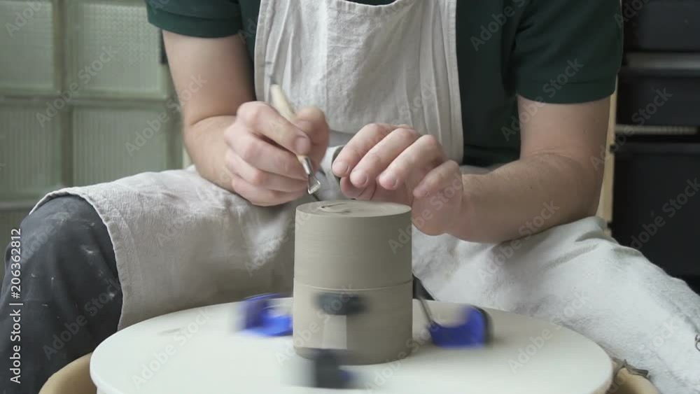 Potter carves a notch on the bottom of the pottery on a rotating circle. With help of a special tool male artisan makes recess of ceramic cup for stability. Potter carves a notch on the bottom of the pottery on a rotating circle. With help of a special tool male artisan makes recess of ceramic cup for stability.