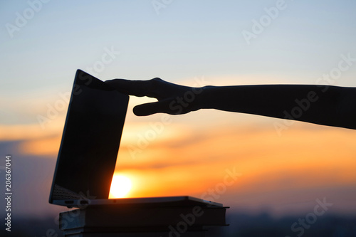 Female hand with laptop on sunset background