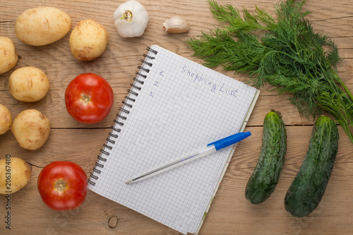 Blank shopping list on paper with vegetables on wooden table