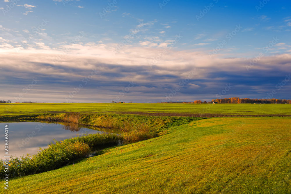 field with lake on sunset in Latvia on cloudy sky background