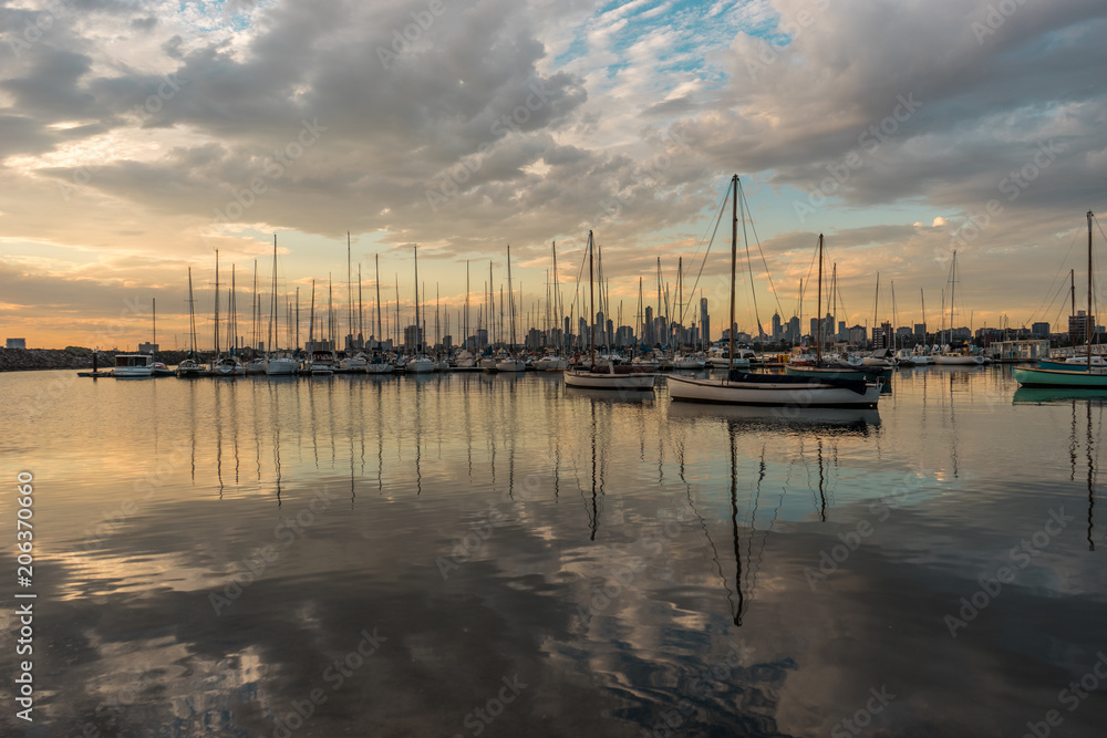 Reflections of many sailing boats with the skyline of downtown in the background. Seen at sunset from St. Kilda Pier in Melbourne, Victoria, Australia (08.04.2018)
