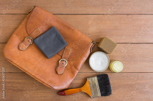 top view of old genuine leather bag on wooden table prepare to clean and care with wax. maintenance concept.