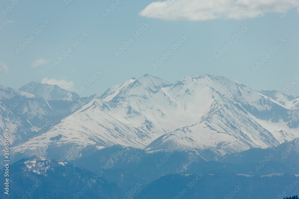 Mountains with peaks covered with snow, white clouds on blue sky, Caucasus