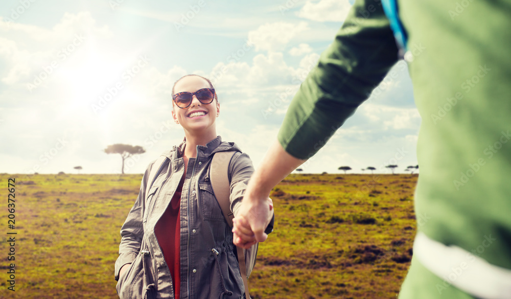 travel, tourism and people concept - happy couple with backpacks holding hands over african savannah background