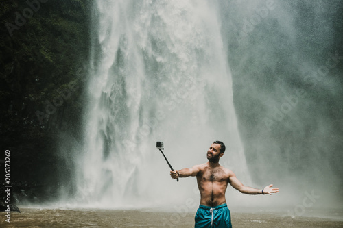 Young handsome tourist visiting the nungnung waterfall in the bali island  indonesia. Having fun in the wild nature. Lifestyle. Travel photography.