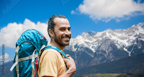 adventure, travel, tourism, hike and people concept - close up of smiling man with backpack over alps mountains background