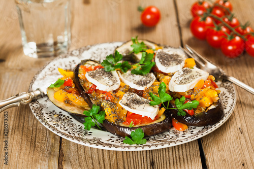 Baked eggplant with yellow and red bell pepper, tomatoes, garlic, goat cheese and chia seeds in plate on an old wooden rustic table