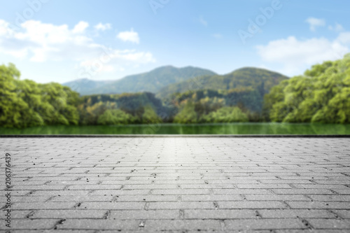 A square made of stone cubes against the background of a green park with a lake and mountains in the background.