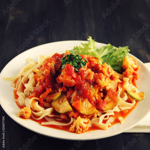 Ribbon pasta with Arrabiata sauce. Close up. Mediterranean dish. Tagliolini pasta with vegetables. Cauliflower, courgette and tomato stew. Italian cuisine. Vegan and vegetarian. Toned photo.