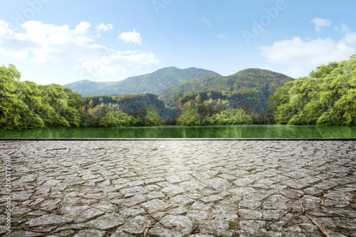 Empty square made of stone cubes against the background of a green park with a lake and mountains in the background.