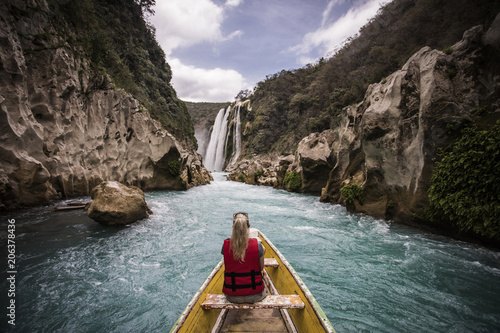 Rear view of woman sitting in boat on river by mountains against waterfall photo