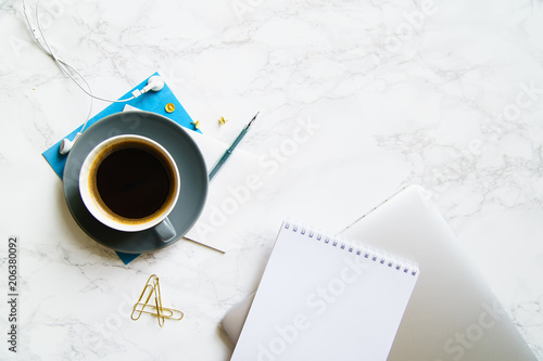 Workplace flatlay with laptop, blue card and coffee cup on marble table