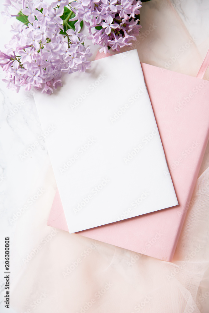 Top vew composition with feminine workspace mock up with empty card, lilac flowers and pink notebook on marble background Top vew composition with feminine workspace mock up with empty card, lilac flowers and pink notebook on marble background
