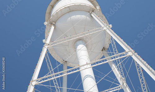 Looking up at a bright white water tower from below with a bright blue cloudless sky. photo