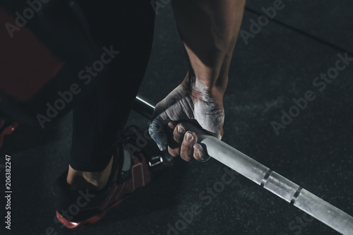 Low section of male athlete lifting barbell in health club photo