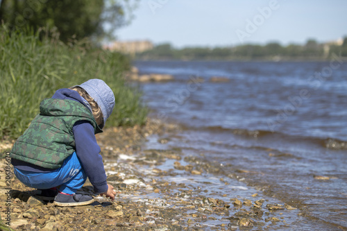 A young boy play close to river under blue sky