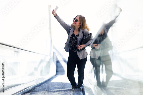 Pretty young business woman taking a selfie with mobile phone in the mechanical stairs.