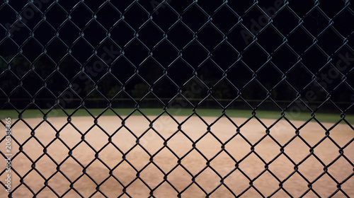 Close up photo of a baseball field fence looking through it to an empty field at night.  Great for background use.