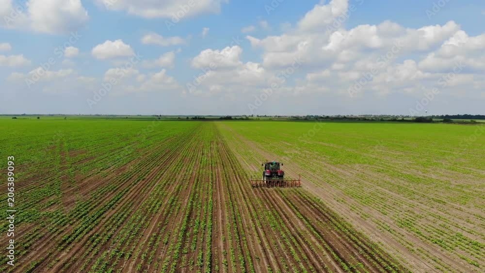 Aerial drone shot of a farmer in tractor cultivating crops on agricultural field, panoramic view landscape farmland sky with clouds Aerial drone shot of a farmer in tractor cultivating crops on agricultural field, panoramic view landscape farmland sky with clouds